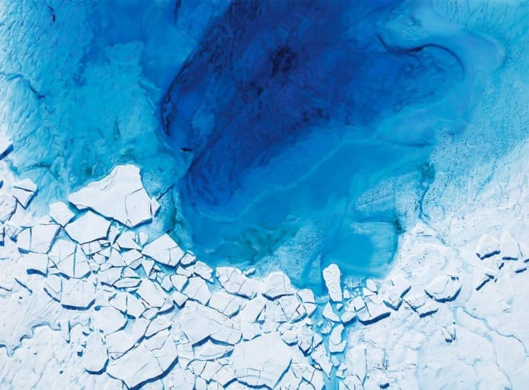 Interview with Zaria Forman on capturing climate change through art Melting glacier with blue ice and cracked surface, aerial view of arctic ice melt, climate change impact on polar regions.