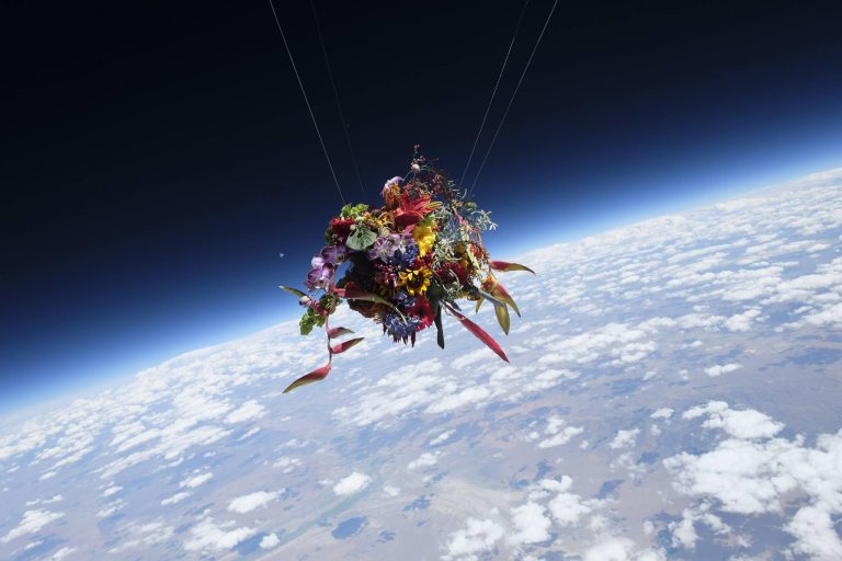 Azuma Makoto Places Delicate Flower Compositions Into Extreme Situations Vibrant floral bouquet floating in space above Earth, surreal art installation in zero gravity environment.