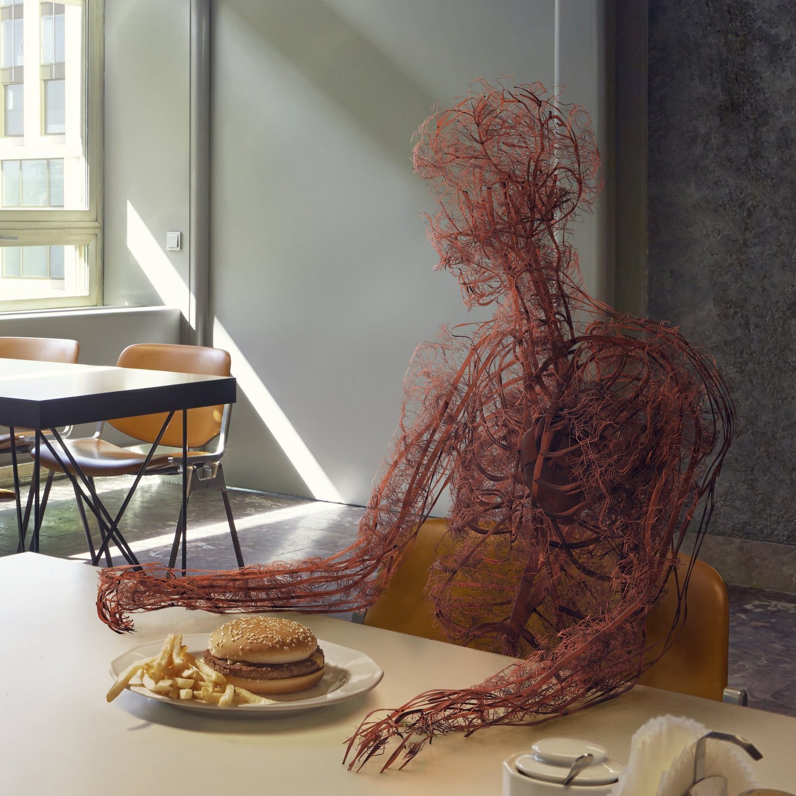 Wired human anatomy sculpture sitting at a table with burger and fries in a modern cafe setting.