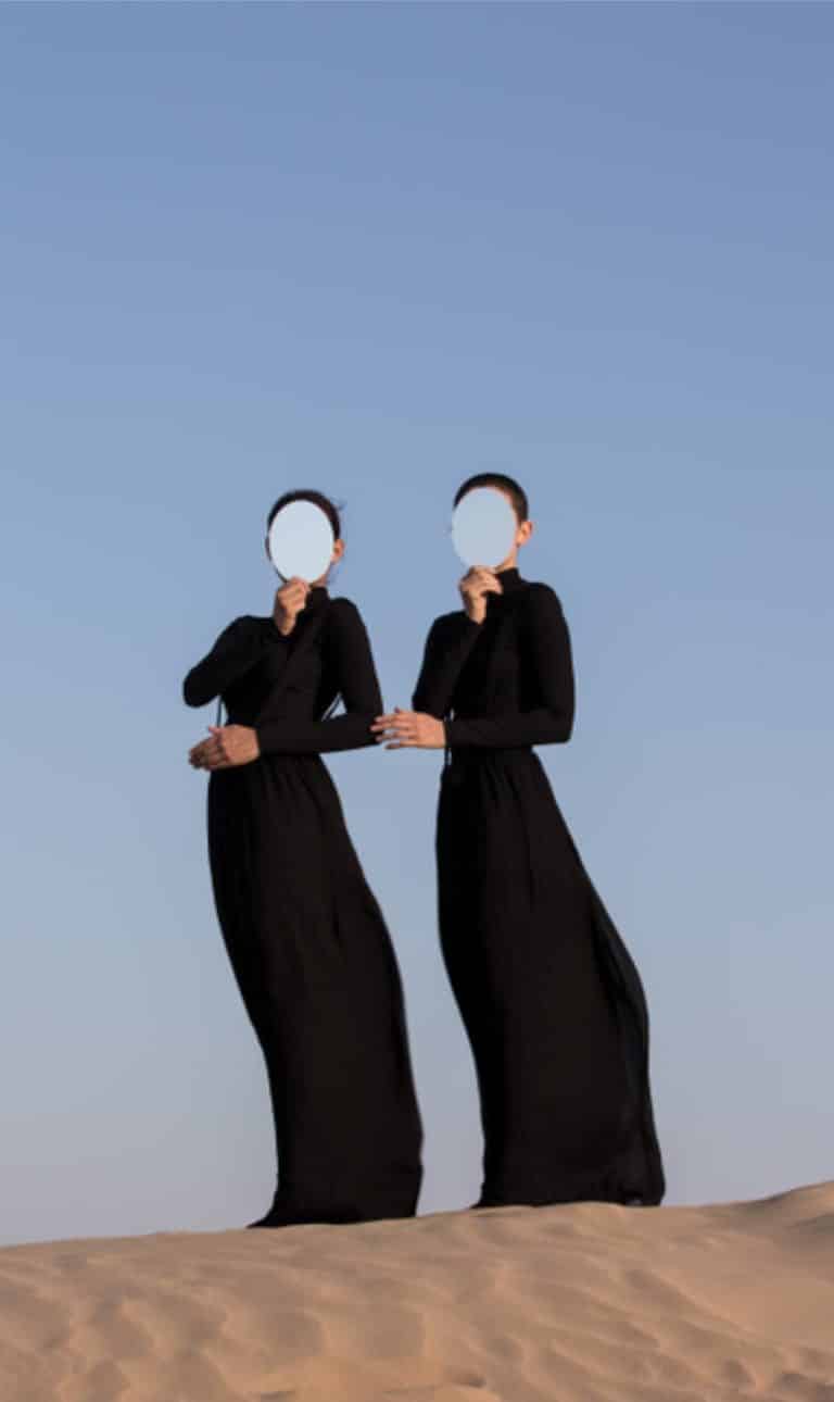 "Mirror Stages And One" Interacts With Dejha Ti The Natural Non-Human Response Ethereal women in black dresses holding mirrors over desert landscape against clear blue sky.