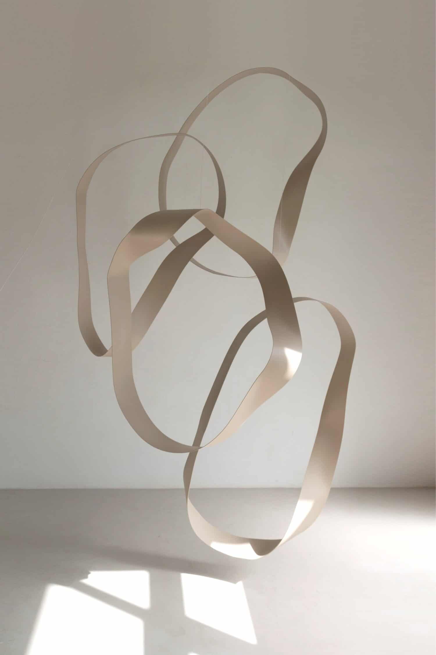 Sculptural modern art installation with intertwined metallic ribbons, minimalist aesthetic.