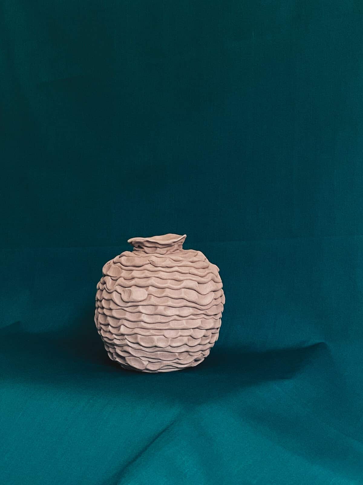 Handcrafted ceramic vase with layered textured surface on teal background.