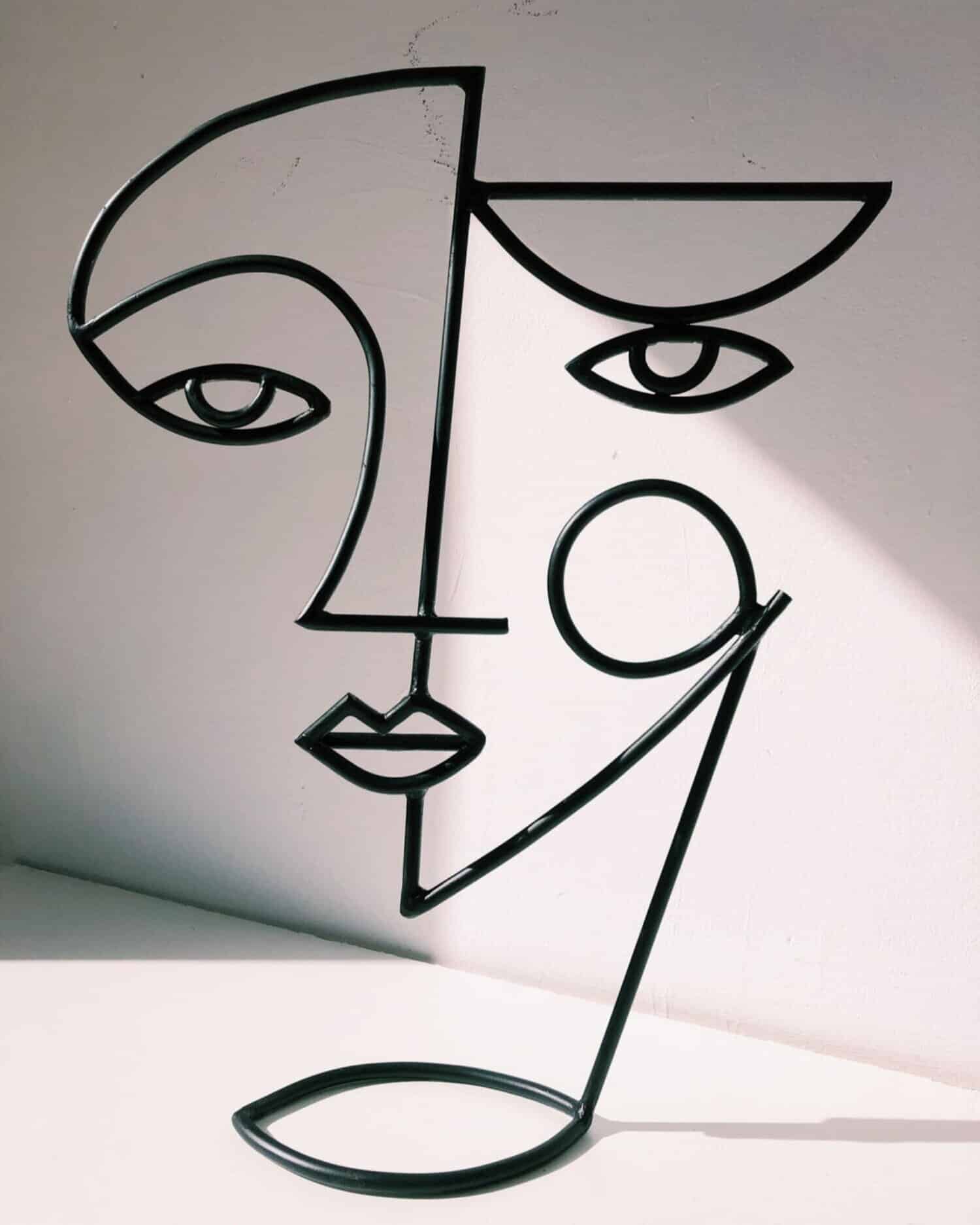 Contemporary abstract metal wall art featuring a minimalist face design with geometric lines and open shapes.