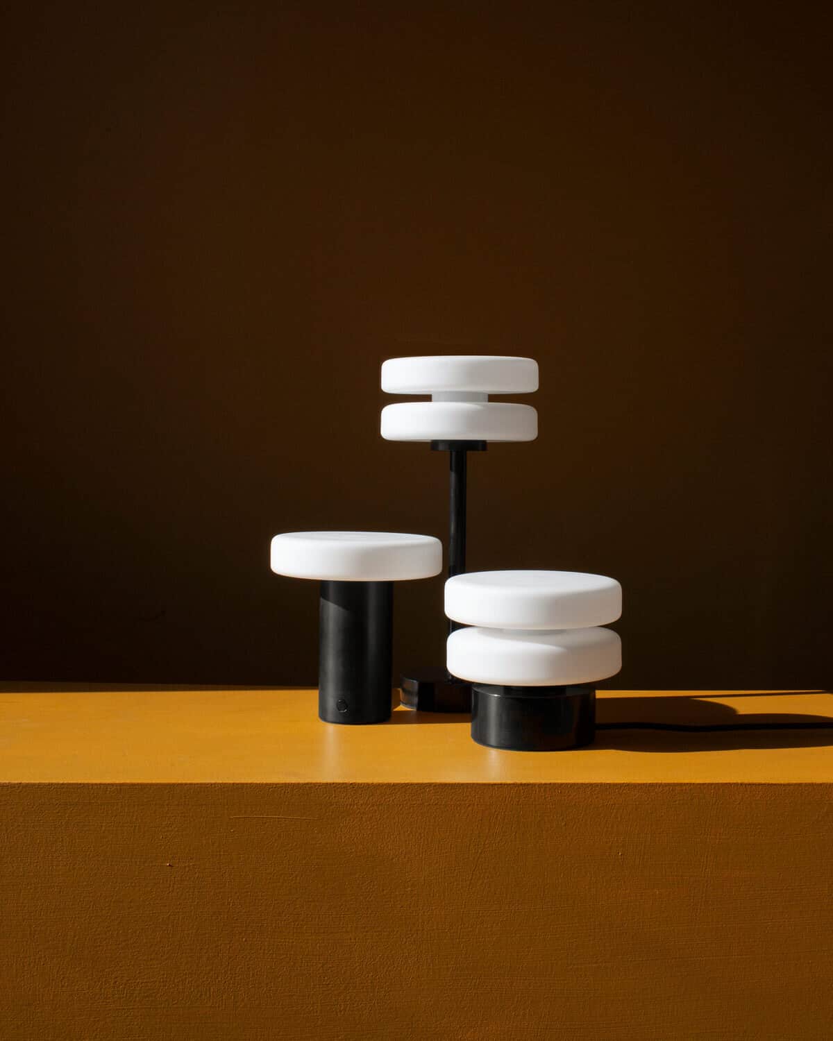 Sculptural modern table lamp with black and white geometric design on mustard-yellow surface.