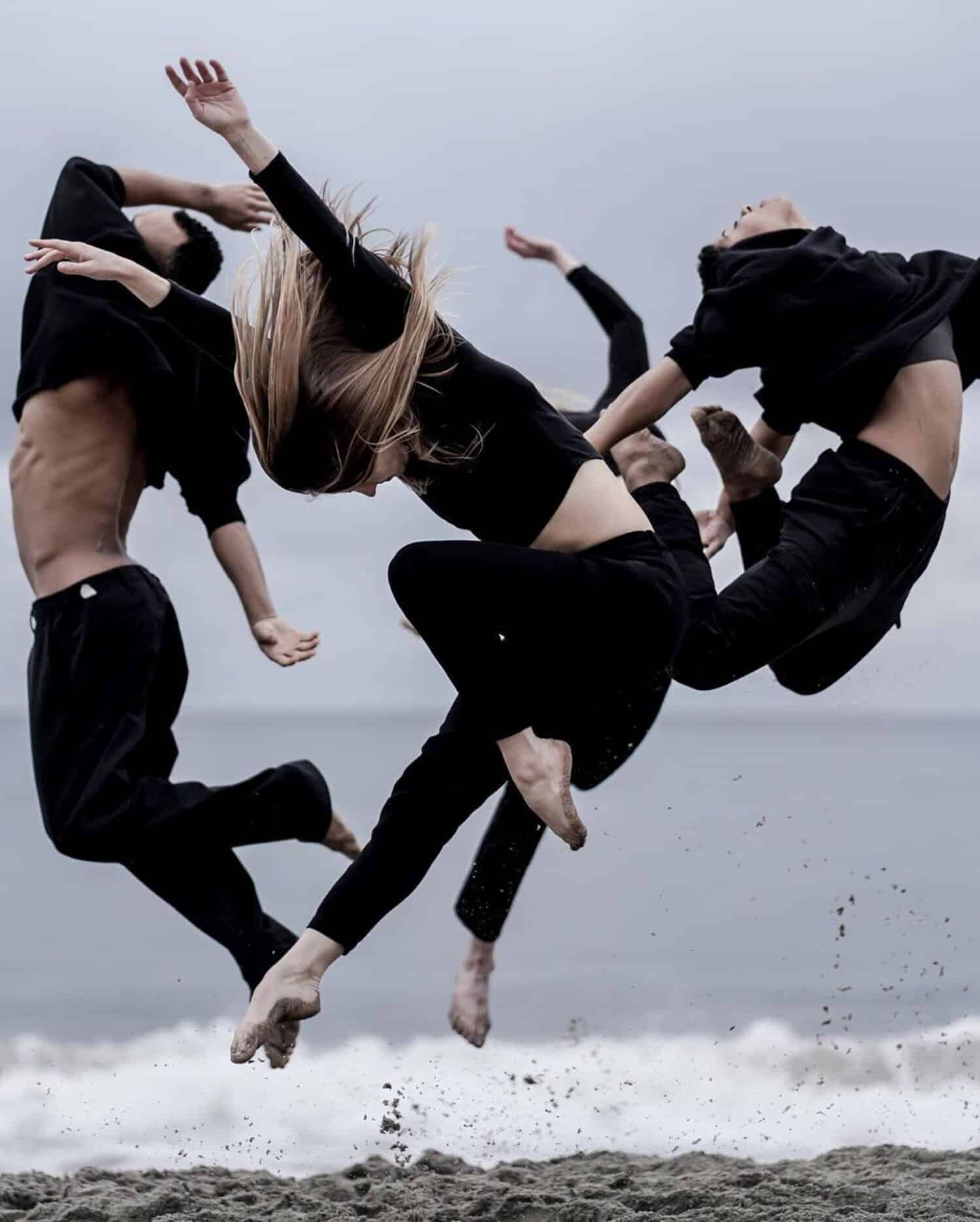 Dynamic contemporary dance performance on the beach with dancers in black outfits mid-air.
