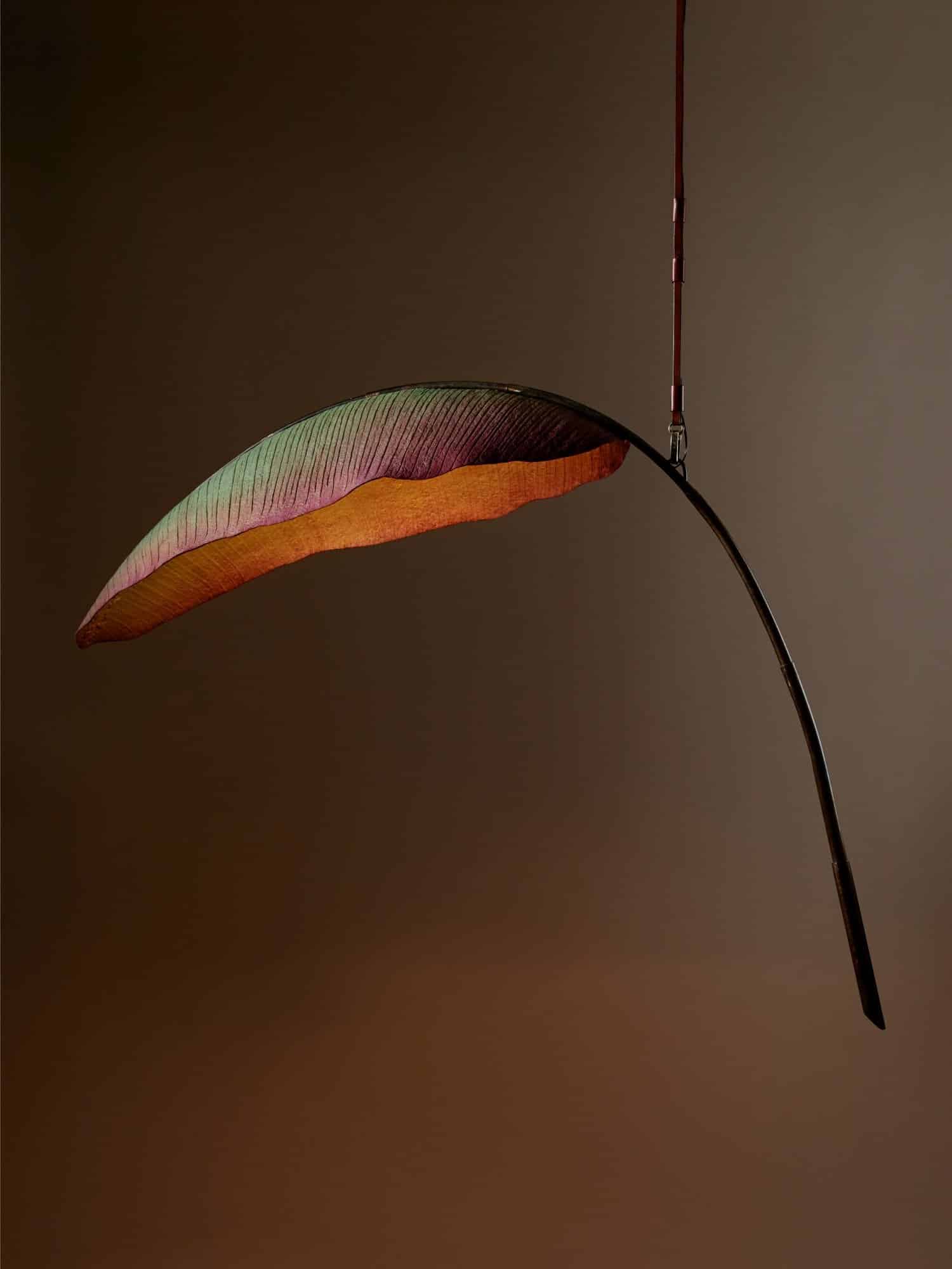 Colorful, modern hanging leaf sculpture with sleek metal support and soft lighting.