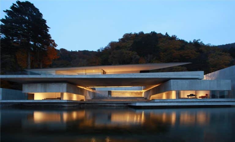 On The Water House By Nikken Sekkei Interconnects Elevated Spaces Modern minimalist concrete house with water reflection and surrounding autumn trees.