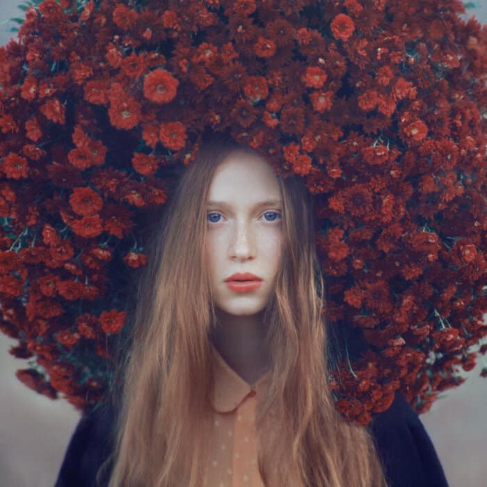 Oleg Oprisco’s Photography Is An Invitation To The Surreal Flower crown with red blooms and young woman portrait, natural beauty, floral headpiece, artistic photography, vibrant colors.