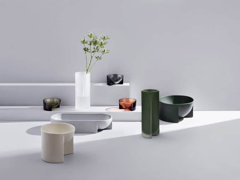 Philippe Malouin's Diverse Design Collections Minimalist modern ceramic bowl and vase set with colored glassware on white display stand.