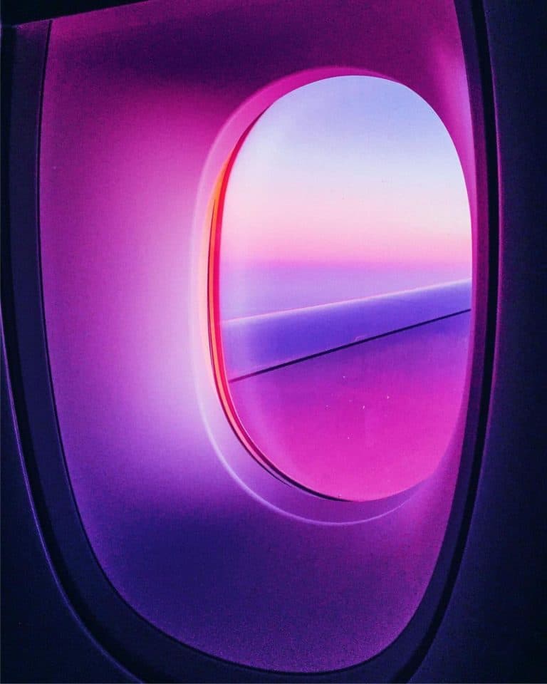 Thibaut Buccellato Captures The Most Prized Sunsets Of A Lifetime Vibrant airplane window with neon pink and purple sunset view, capturing a futuristic and artistic travel scene.