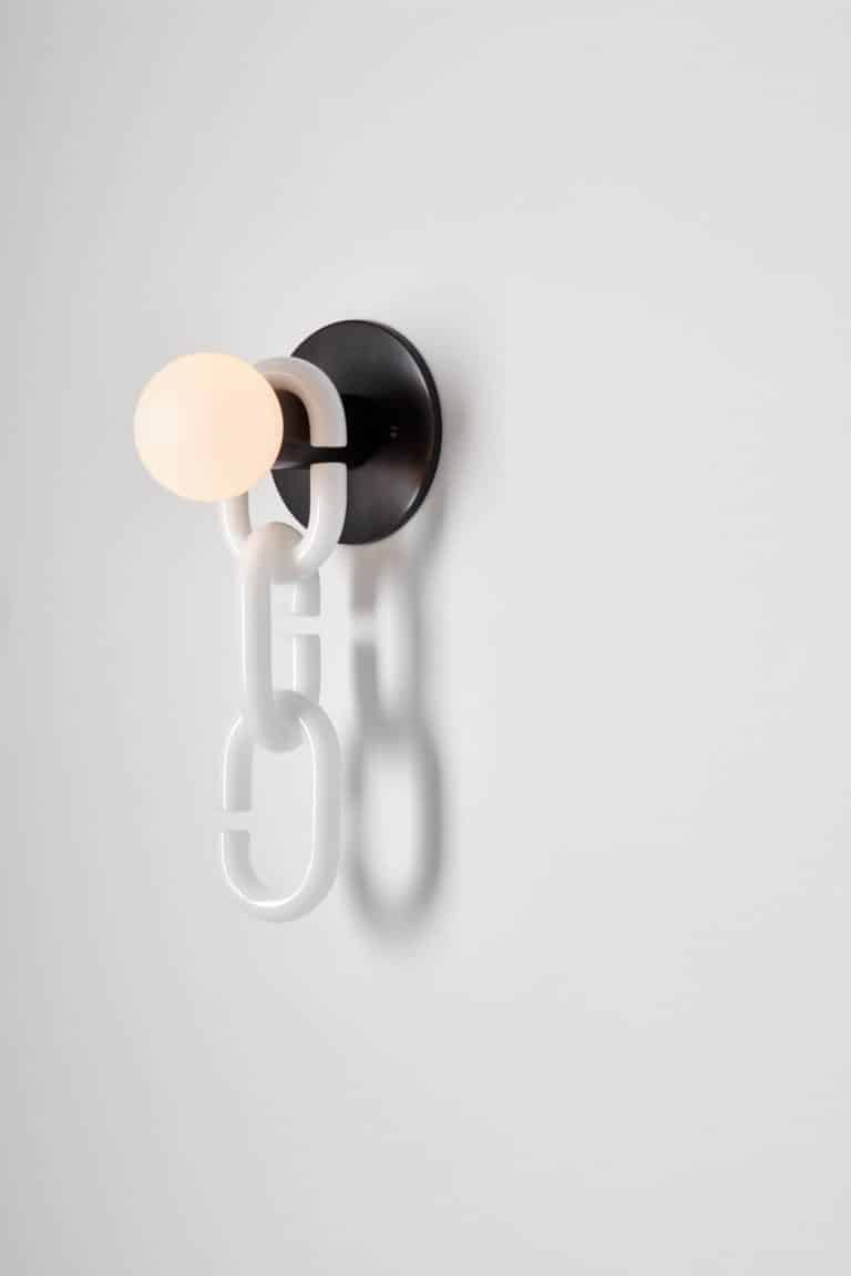 Trueing’s Glassy Lighting Collection Debuts At Pas De Calais SoHo Flagship Minimalist modern wall sconce with white chain and glowing bulb, contemporary interior lighting design, visual atelier 8 style.