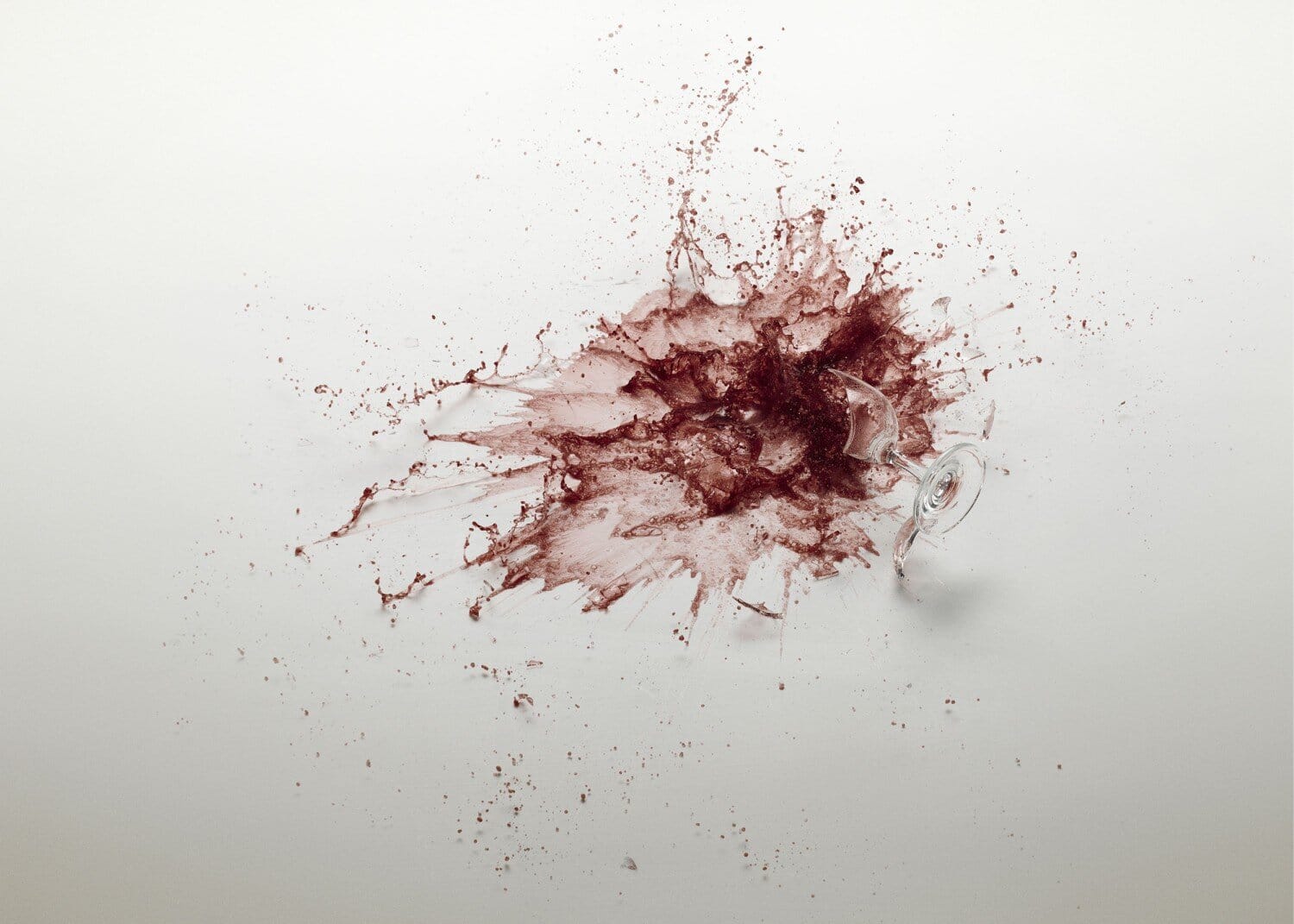 Crushed glass and wine splatter on white background, artistic composition, high-resolution macro shot.