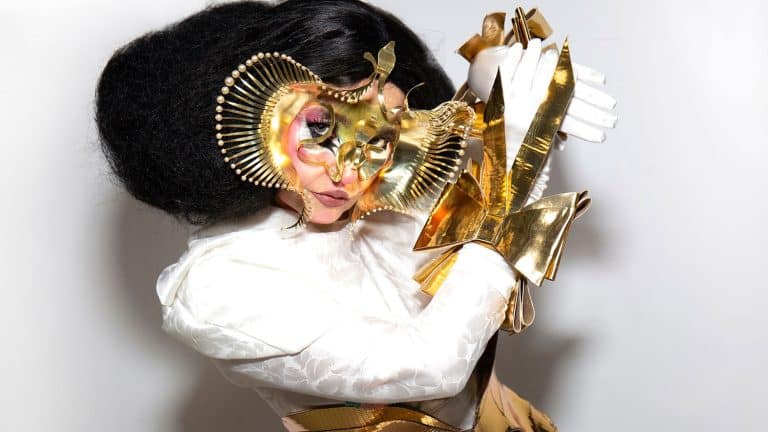 Intricate gold Venetian mask with black hair and white gown, artistic fashion statement for carnival or event.