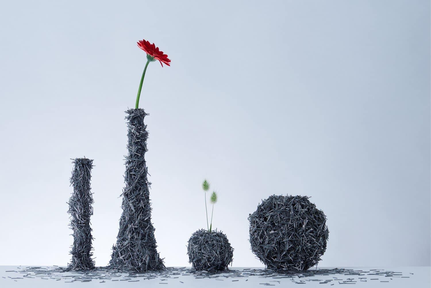 Hand sculpture made of nails holding a red flower and small plants on a plain background.