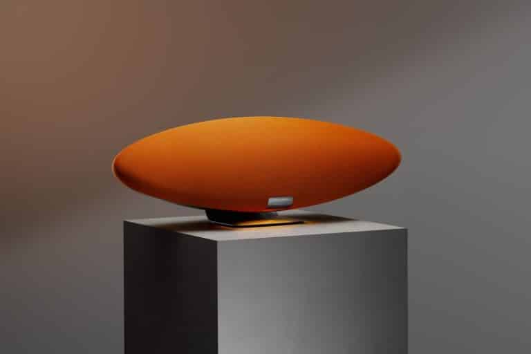 Introducing the Zeppelin McLaren Edition: Fusion of Iconic Design and Superior Sound Luxurious orange oval speaker with fabric cover on display at Visual Atelier 8 exhibition.