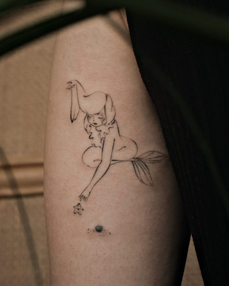 The Cultural Symphony of Ningjia Zhai's Illustrated Narratives Delicate line art tattoo of a mermaid with a pony on her head and leaf tail on arm, black ink on light skin.