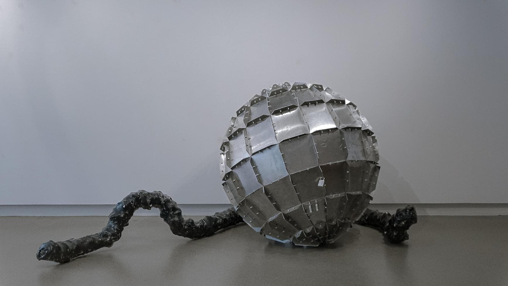 Chromed geometric sculpture resembling an atom or virus structure placed on a neutral surface.