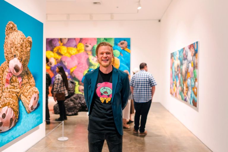 Artist Brent Estabrook's Captivating Technicolor Plushies, Pop Ups, and Books Colorful teddy bear artwork displayed at Visual Atelier 8 art gallery with a smiling man in front.