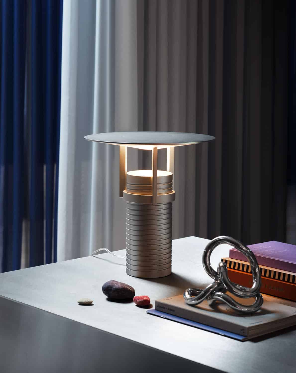 Modern ceramic table lamp with sculptural design and soft lighting, decorative books and stones on white surface.