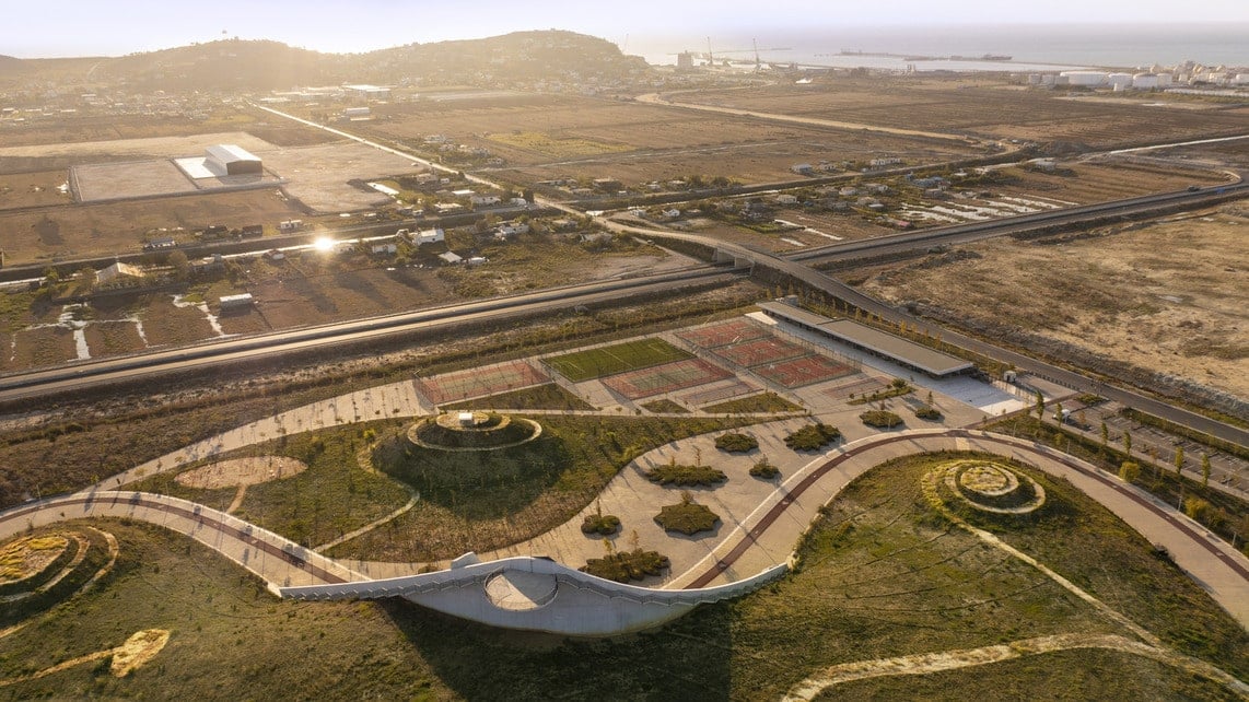 Aerial view of eco-park with winding paths, greenery, and distant farmland at sunset.