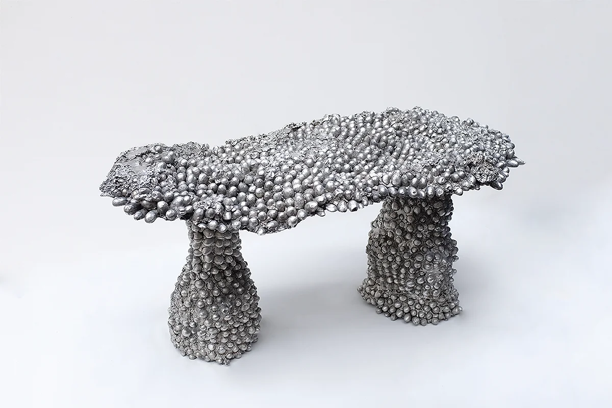 Shiny metallic sculpture of a bench made from numerous small silver balls.