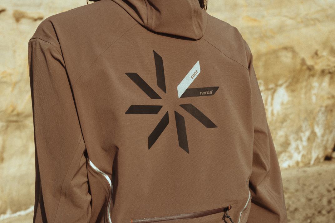 Reflective outdoor brown jacket with geometric logo design, ideal for hiking and outdoor activities, by Visual Atelier 8.
