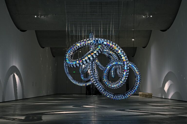 An interview with Yunchul Kim on exploring the transformative nature of matter Colorful glass art installation of intertwined luminous loops in a modern gallery space.