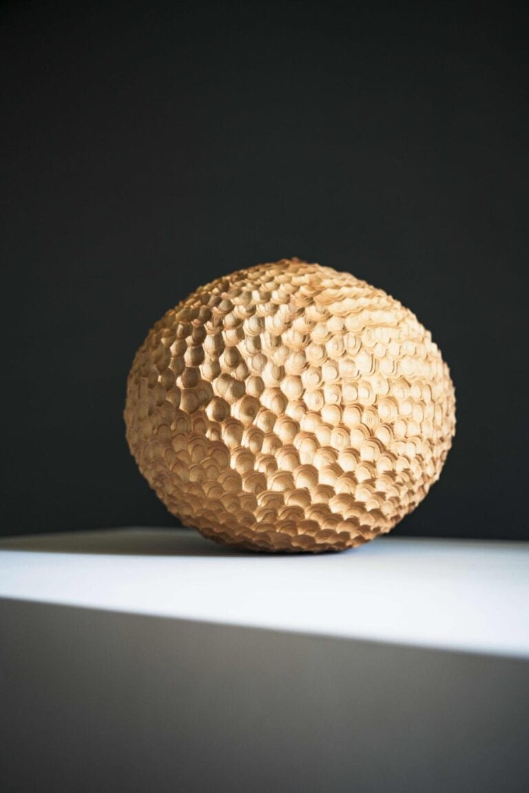 Oliver Chalk artistry reflecting a deep connection to texture and nature Wooden geometric sphere sculpture with textured honeycomb surface.