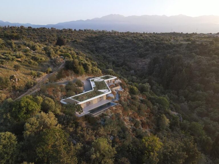 Modern hillside home with sleek architectural design in a lush green mountain landscape.