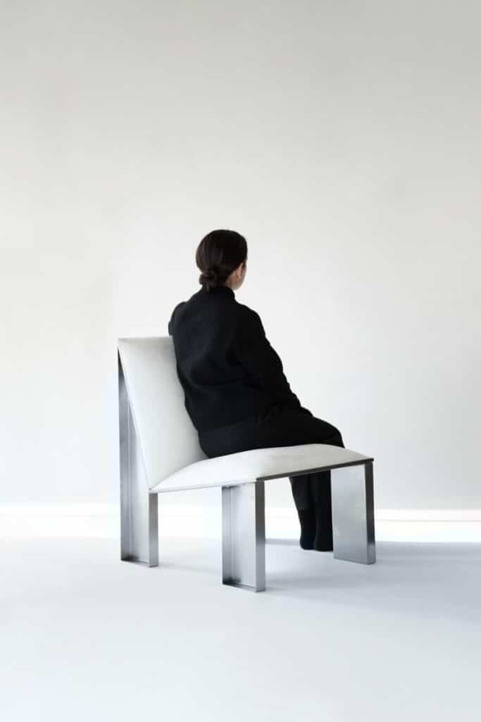 Minimalist modern black and white woman sitting on sleek metal and white chair in contemporary interior.