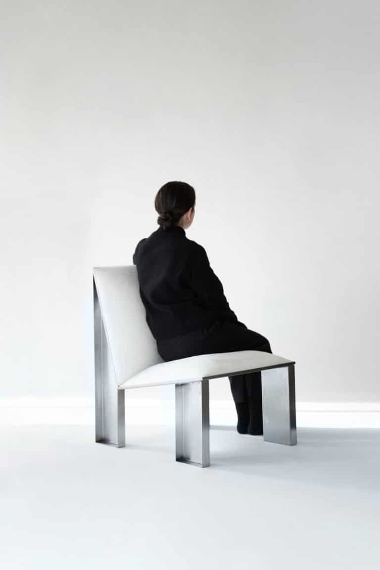 ELE Armchair: A timeless fusion of craft and imagination by Jaume Ramírez Minimalist modern black and white woman sitting on sleek metal and white chair in contemporary interior.