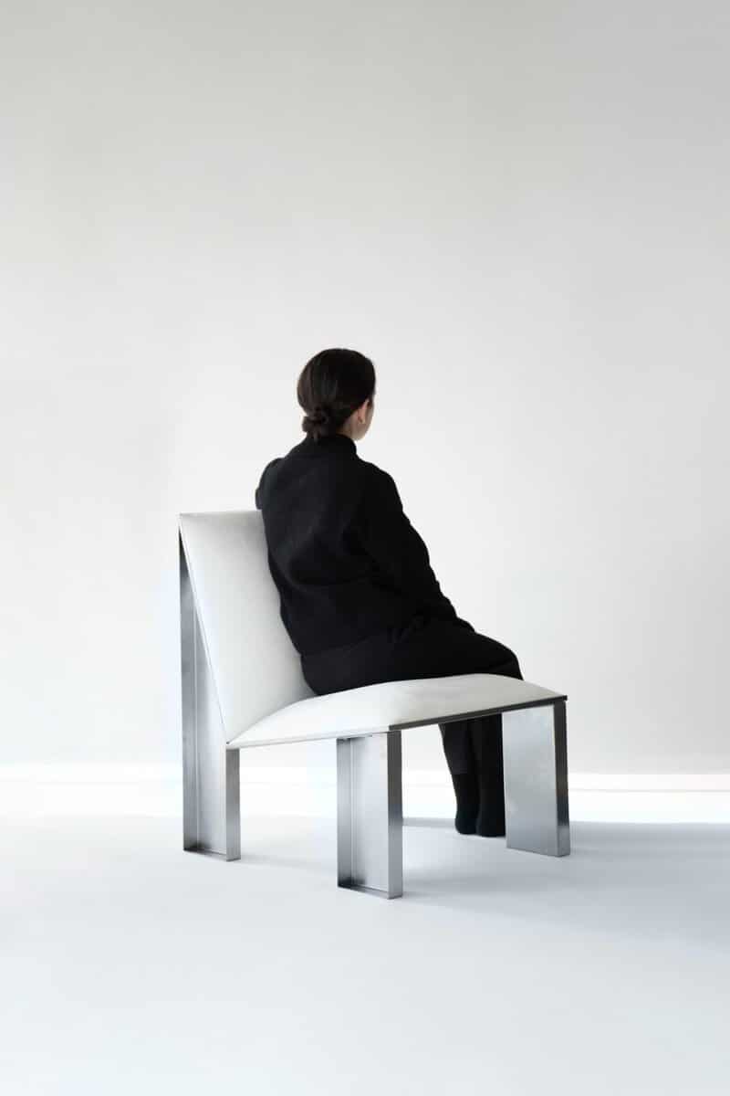Minimalist modern black and white woman sitting on sleek metal and white chair in contemporary interior.