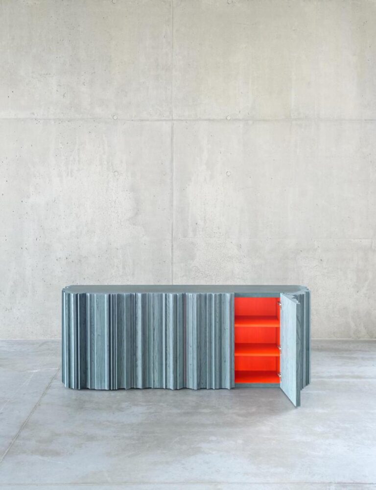 YKB collection by Jiri Krejcirik blending modernism and craftsmanship Contemporary metal storage cabinet with orange interior shelves against minimalist concrete wall.