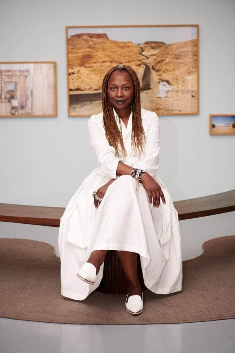 Koyo Kouoh appointed artistic director of Venice Biennale 2026 Vintage-inspired white dress woman seated in contemporary art gallery.