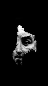 Framed white clay sculpture of a human face on black background.