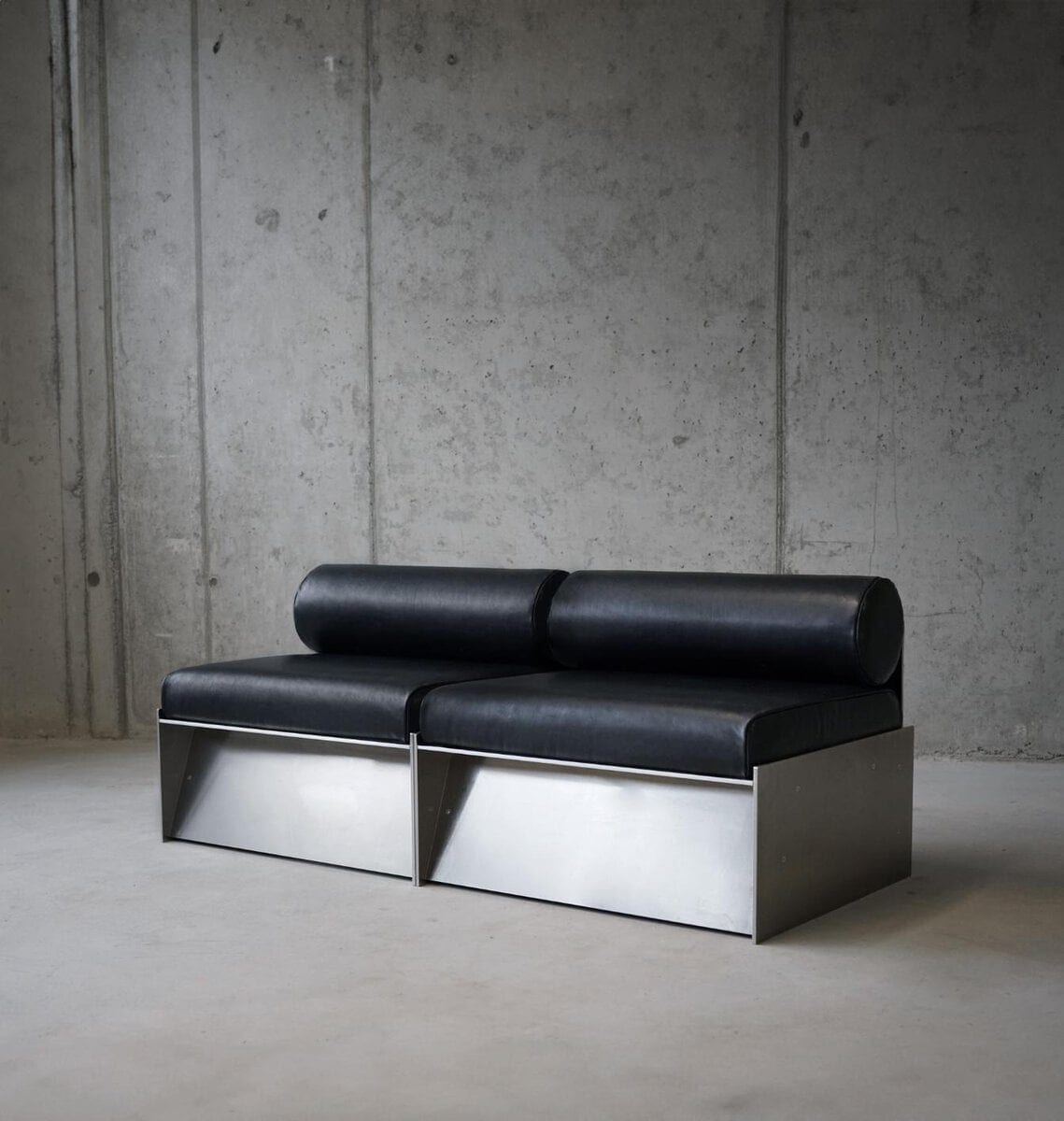 Sleek modern black leather sofa with stainless steel base in minimalist industrial setting.