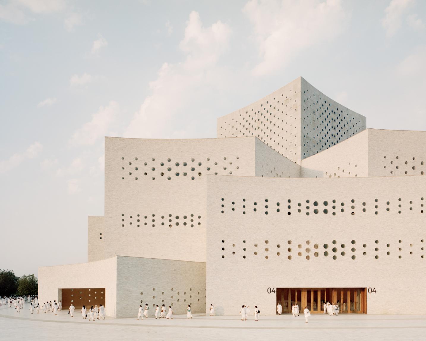 Modern architectural building with perforated white concrete facade, minimalistic design, and even lighting.