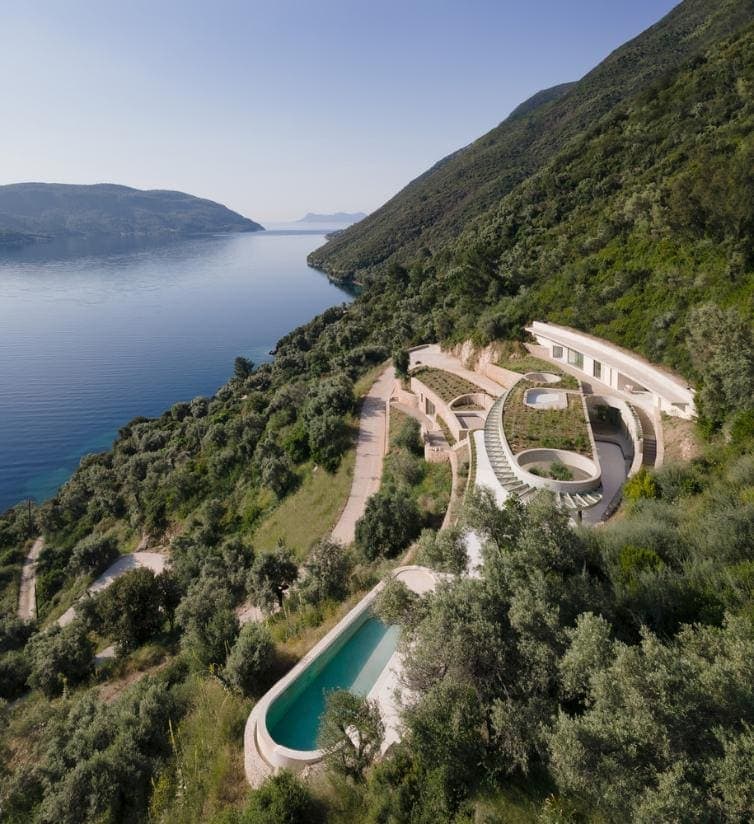 THYTA House offers breathtaking views and serene outdoor spaces Modern hillside villa overlooking a lake with infinity pool and lush greenery.