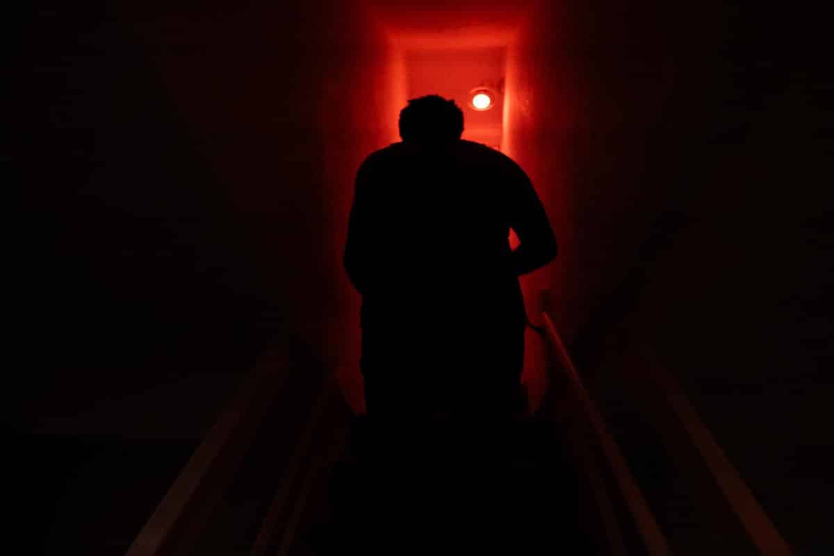 A person ascending stairs in a dark corridor illuminated by red lighting.