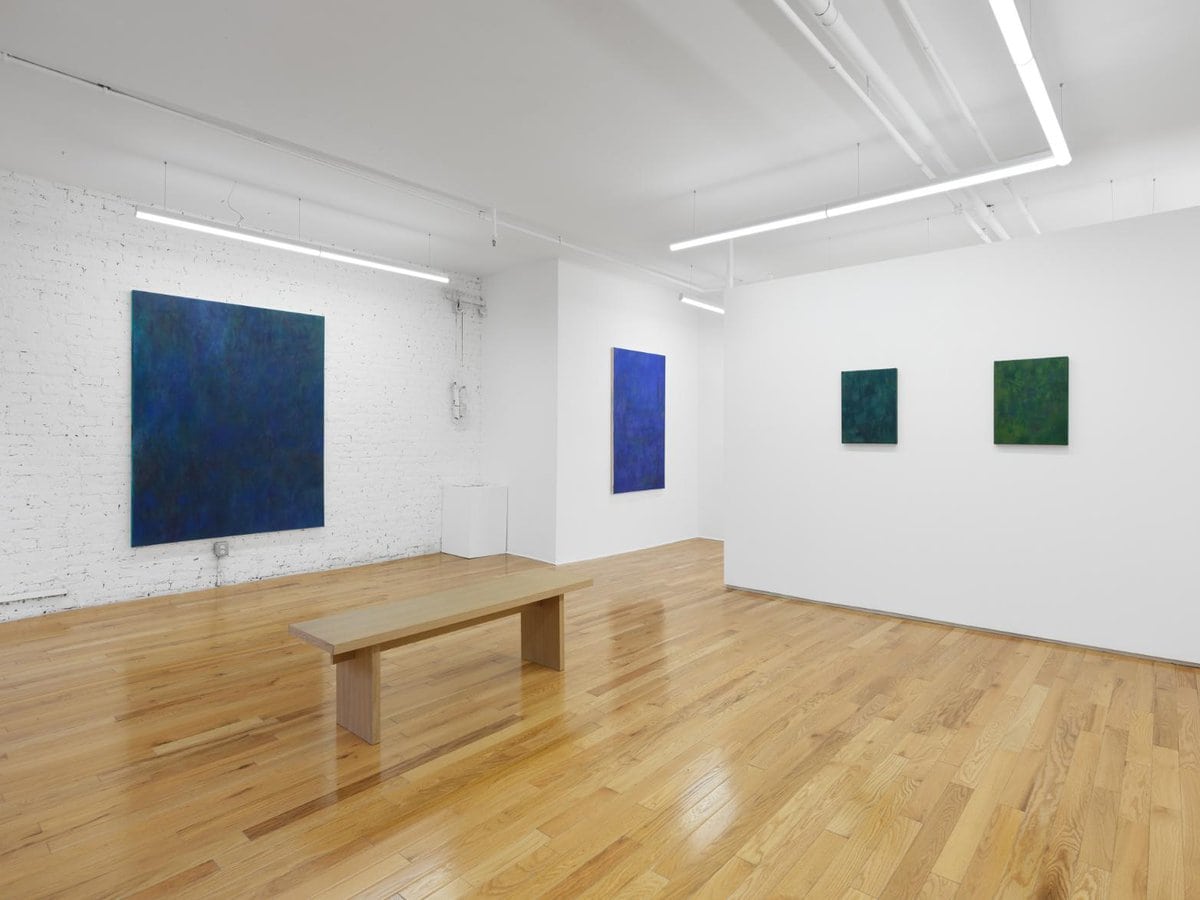 Vibrant blue and green abstract paintings in modern art gallery with wooden floor and minimalist lighting setup.