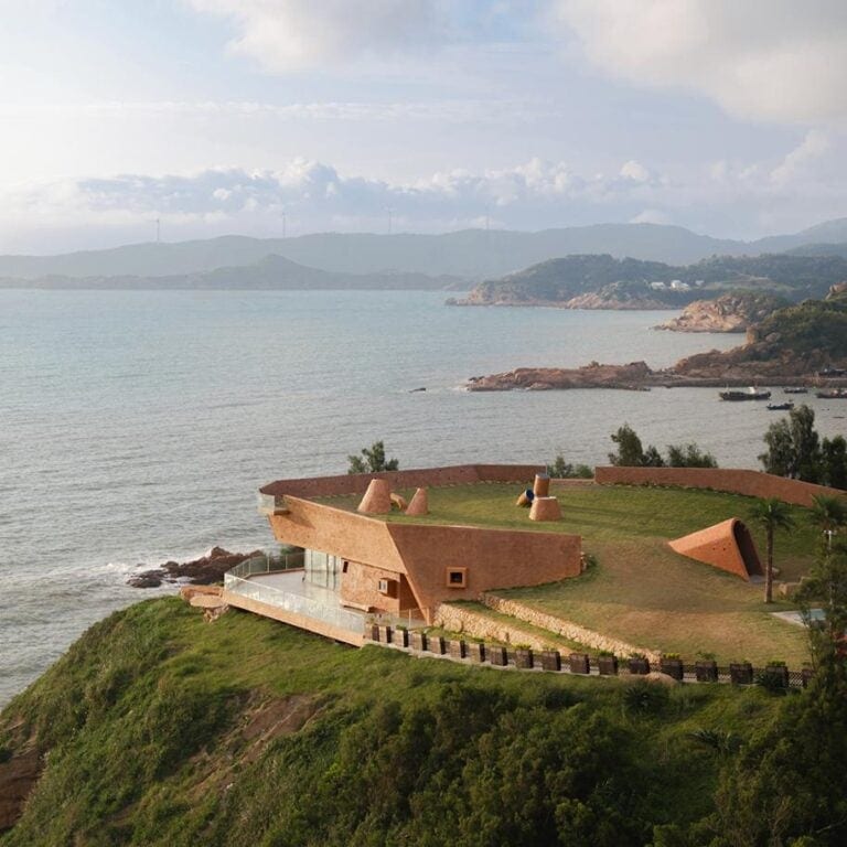 Blue Insight Cave Space: A sustainable architectural gem by the East China Sea Unique modern house on a hillside overlooking the ocean with scenic coastal views and lush greenery in the background.