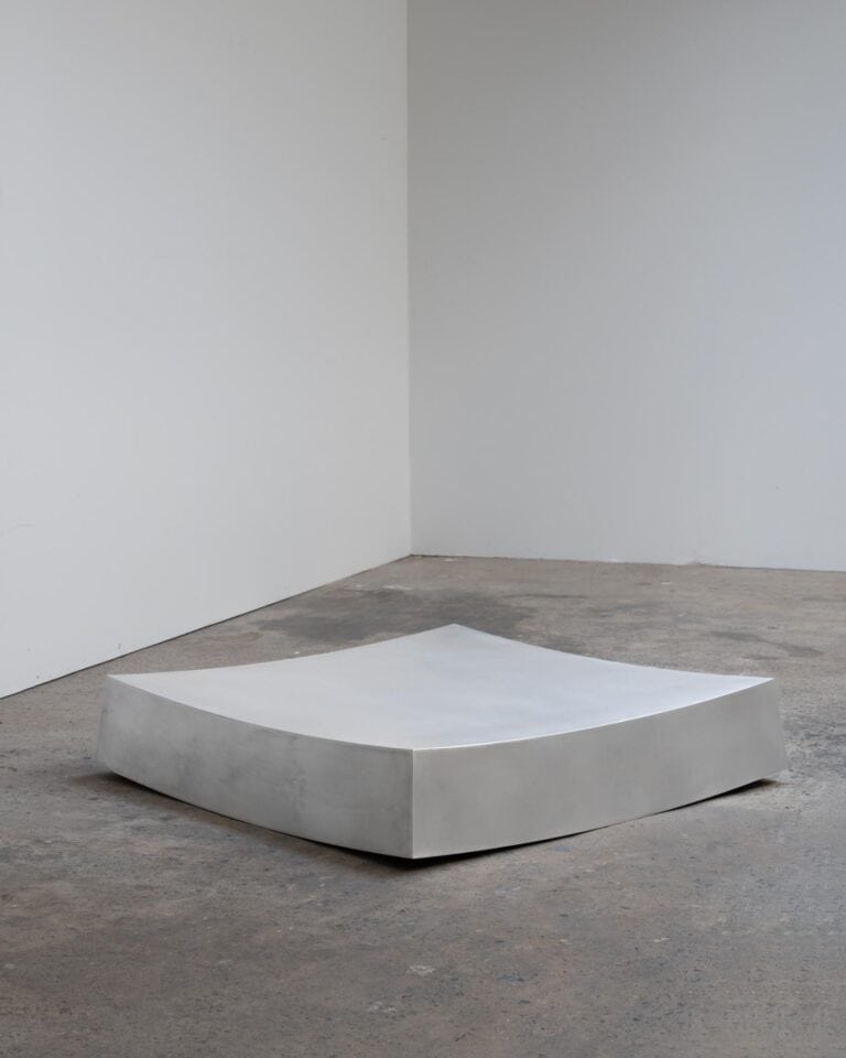 Vormen's Curved Low Table emphasizes form and stability Minimalist concrete sculpture on raw concrete floor, modern art installation in gallery setting, monochrome neutral tones.