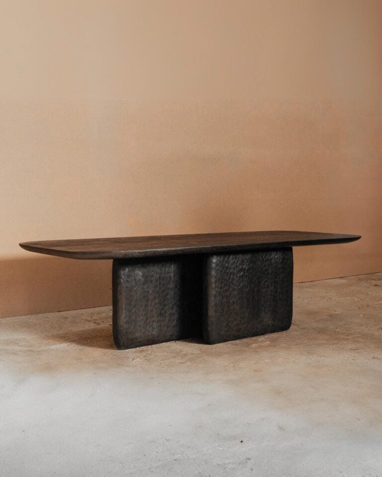 Darling Dining Table by Dennis Kaiser: Handcrafted Elegance from Tuscany Contemporary black wooden bench with textured surface, modern minimalist design, placed on neutral concrete floor.