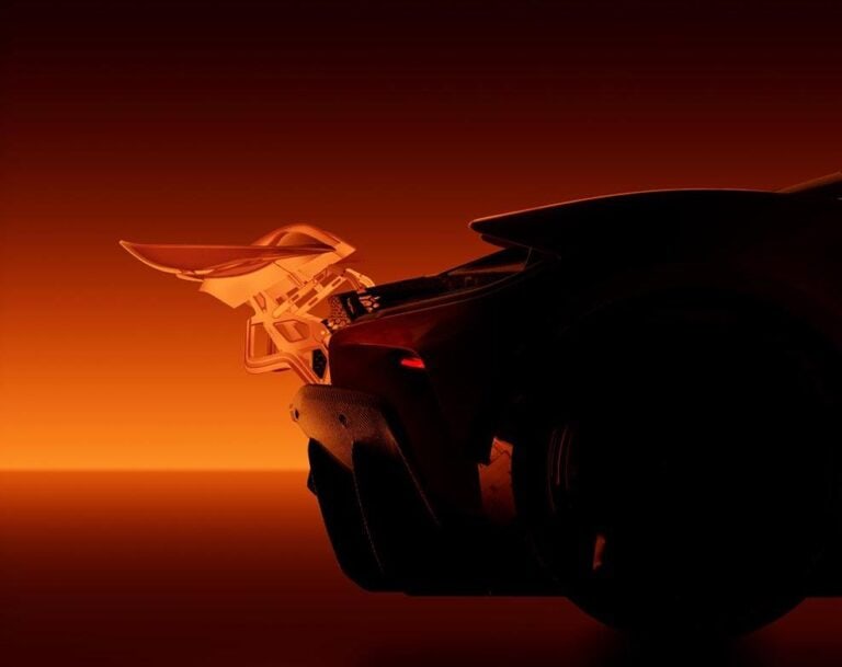 McLaren and Richard Mille at full speed towards mechanical emotion Sleek black sports car with aerodynamic design and rear spoiler illuminated by warm orange lighting.