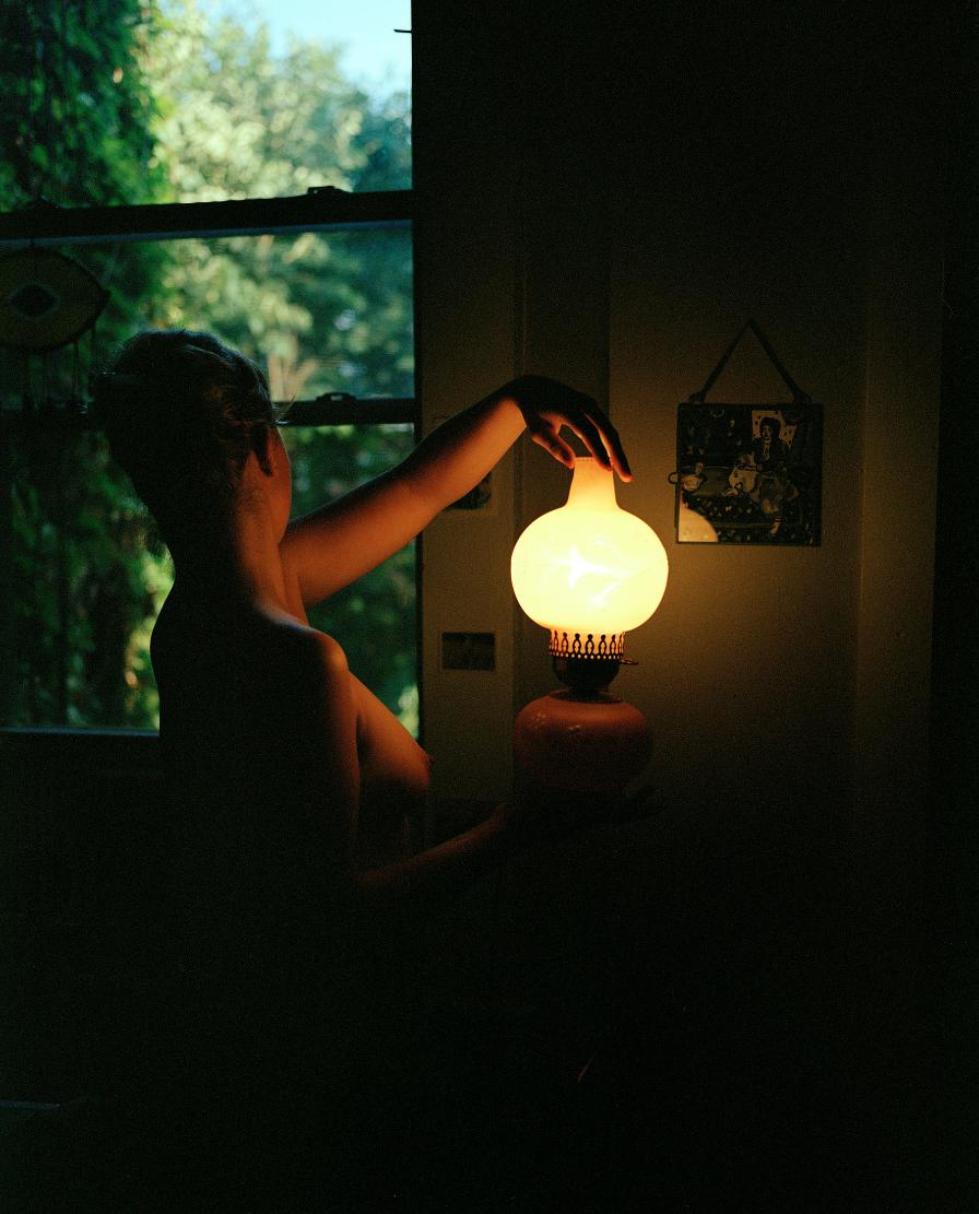 Warm interior lighting with vintage lamp in a cozy space, silhouette of a woman, natural outdoor view, artistic photography.