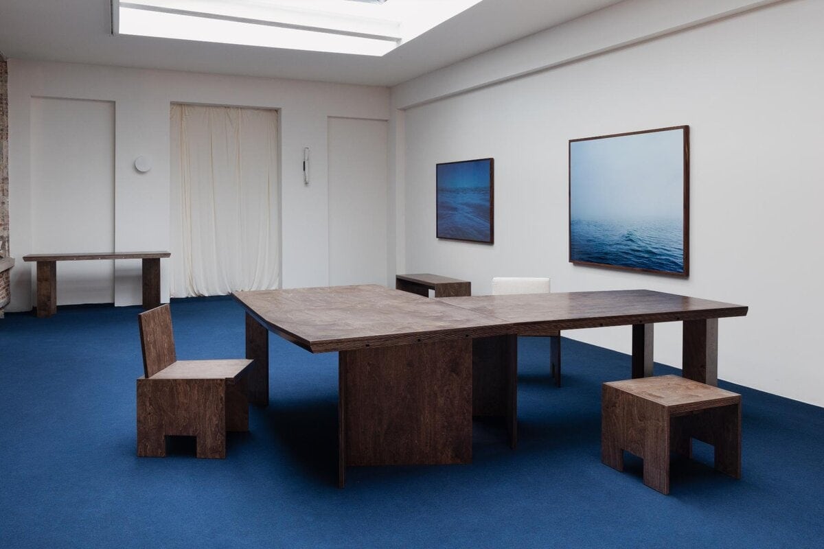 Minimalist art gallery with wooden tables and ocean-themed framed artwork - clean, modern interior design.