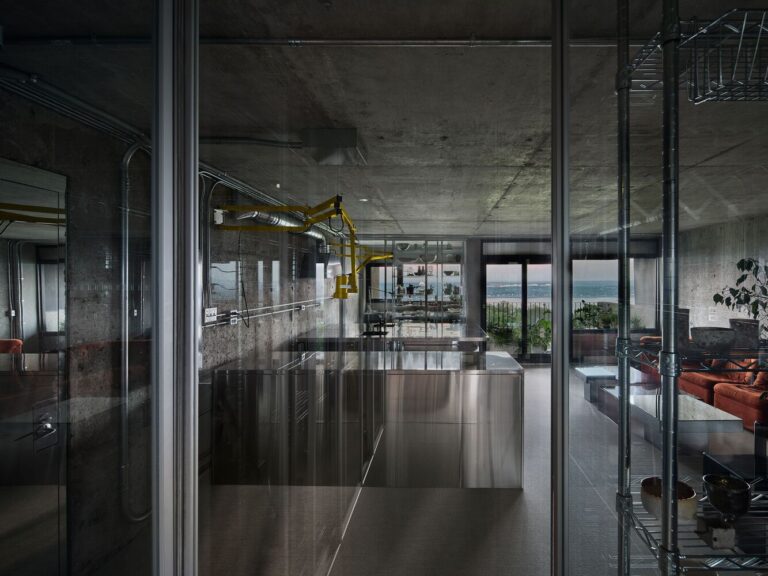 Studio Jean Verville's brutalist exploration of modular living in Bruj Stainless steel kitchen with modern industrial design, concrete walls, large windows, and city view.