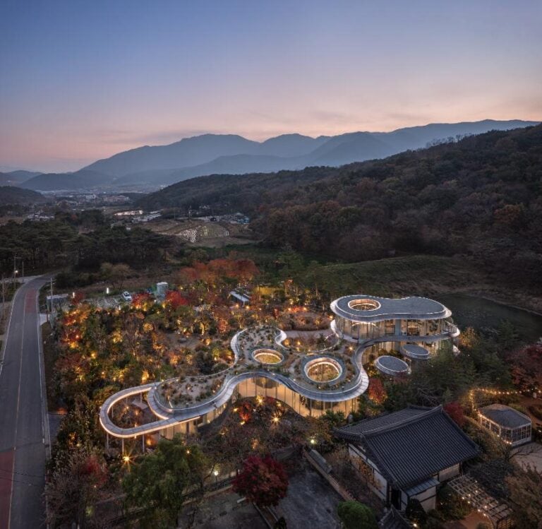 MIGIUI by Architect-K, a soulful café in the heart of Ulsan Modern architectural building with organic shapes surrounded by autumn foliage and mountain landscape at dusk.