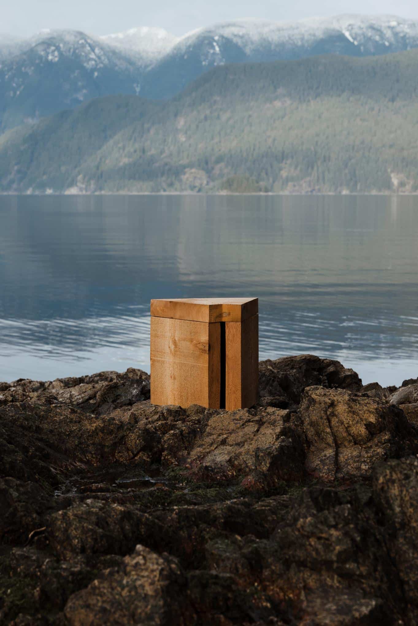 Wooden outdoor sculpture on rocky shoreline with mountain lake background.