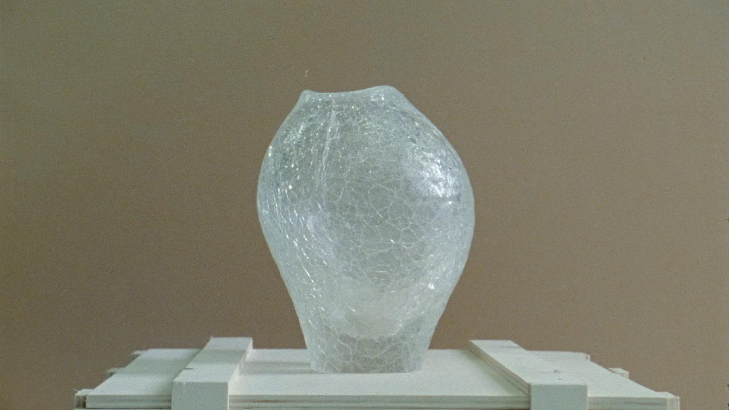 Cracked glass vase sculpture placed on a white display stand.